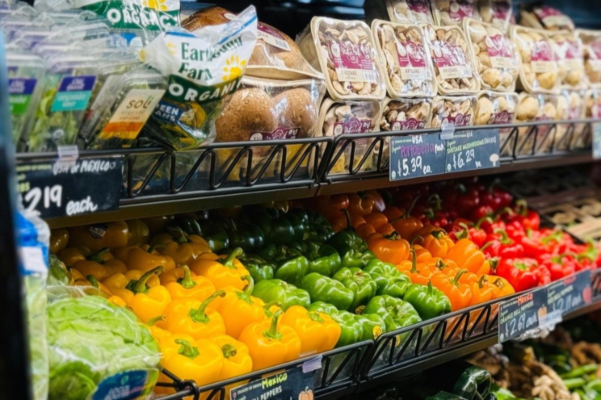 two rows of produce at a grocery store, including bell peppers, mushrooms, and herbs