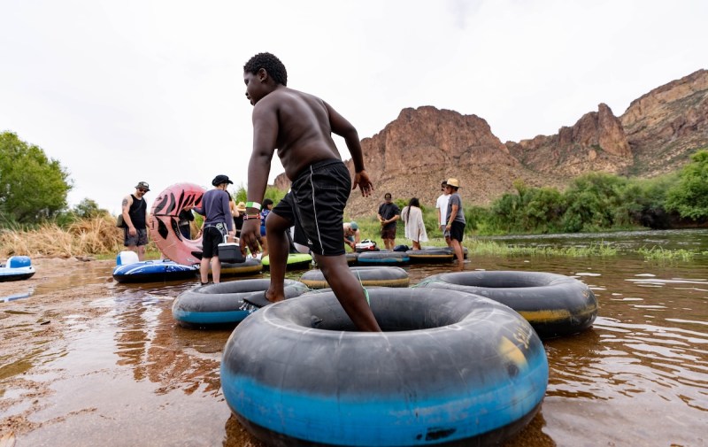 a group of people standing in the shallow part of a river with inner tubes floating on the surface