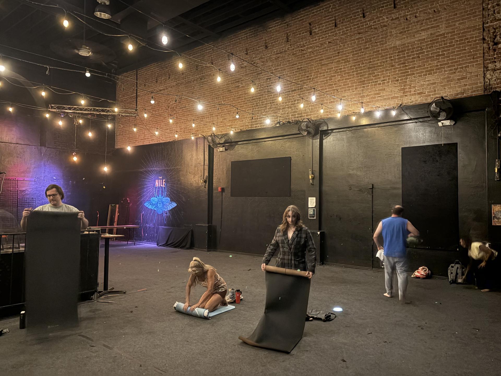people rolling up yoga mats in a room with string lights along the ceiling