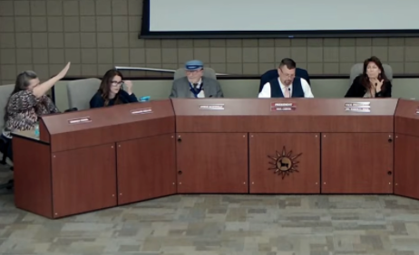 image of five people seated at long table with woman on the left holding arm up in a Nazi salute