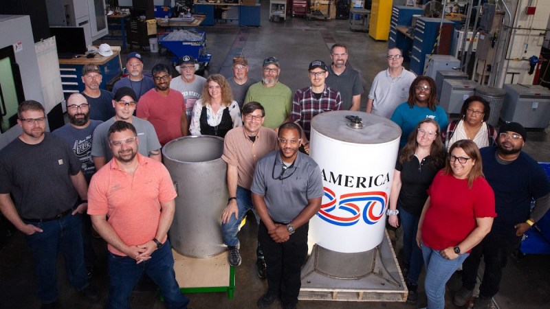 a group of people standing around a white time capsule