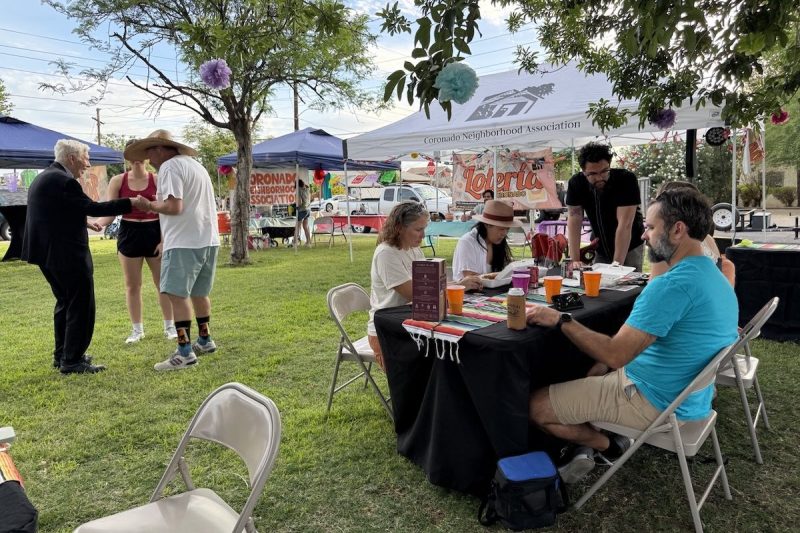 people standing and sitting at tables in a street fair setting