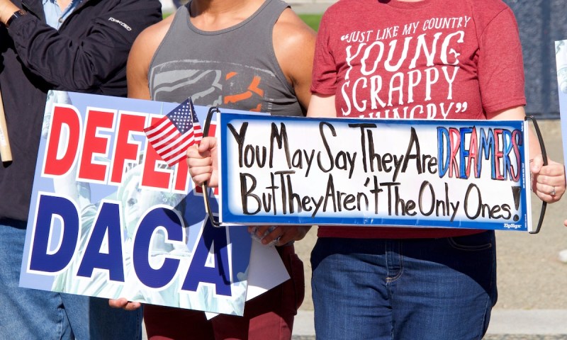 people holding signs that say "Defend DACA" and "you may say they are Dreamers but they aren't the only ones!"