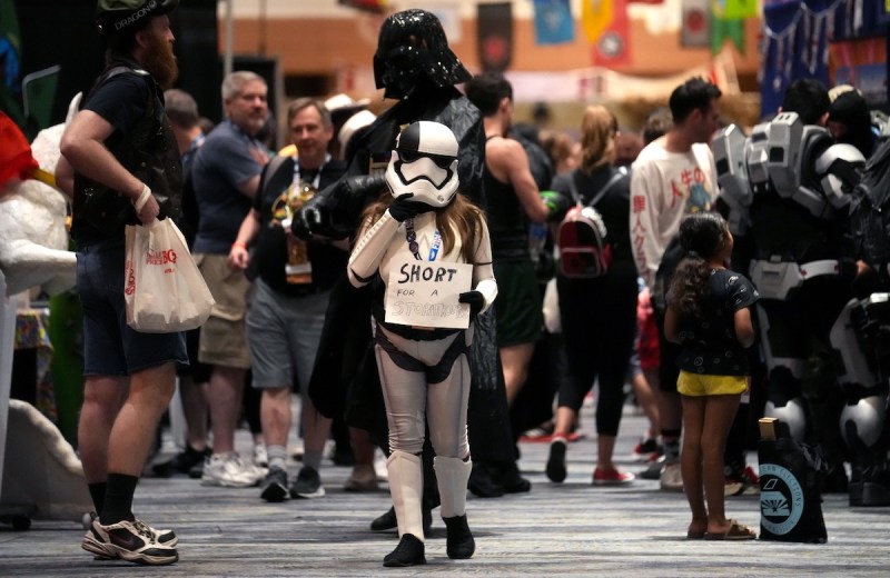 a crowd of people walking through a hallway with the focus on a girl wearing a Stormtrooper outfit holding a sign that says short for a Stormtrooper