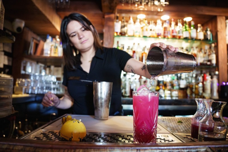 woman pouring liquid from cocktail shaker into a glass at a bar