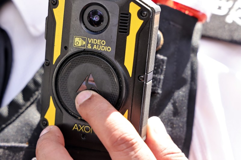 close up on an Axon body camera that someone is wearing, with their finger hovering over the camera