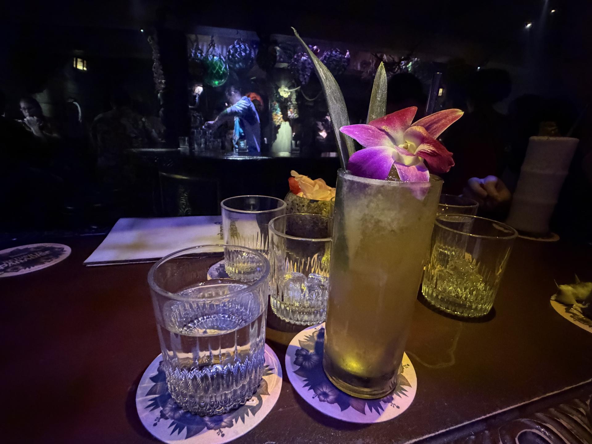 a glass of water and a cocktail with a flower in it on a table