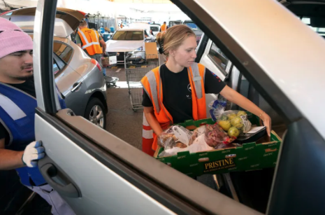 a woman in a safety vest putting a box full of produce into a car