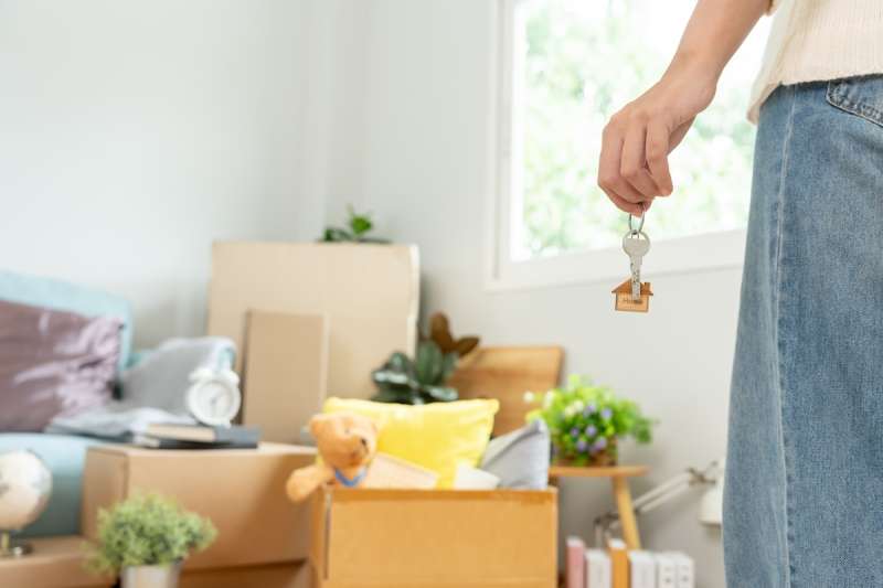 part of a woman's body holding a key in her hand while in the background there are moving boxes against a wall