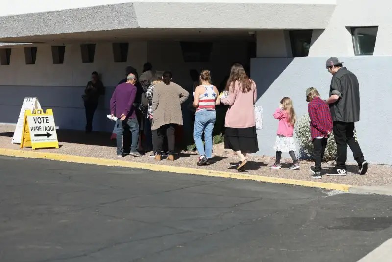line of people outside a building next to a vote here sign