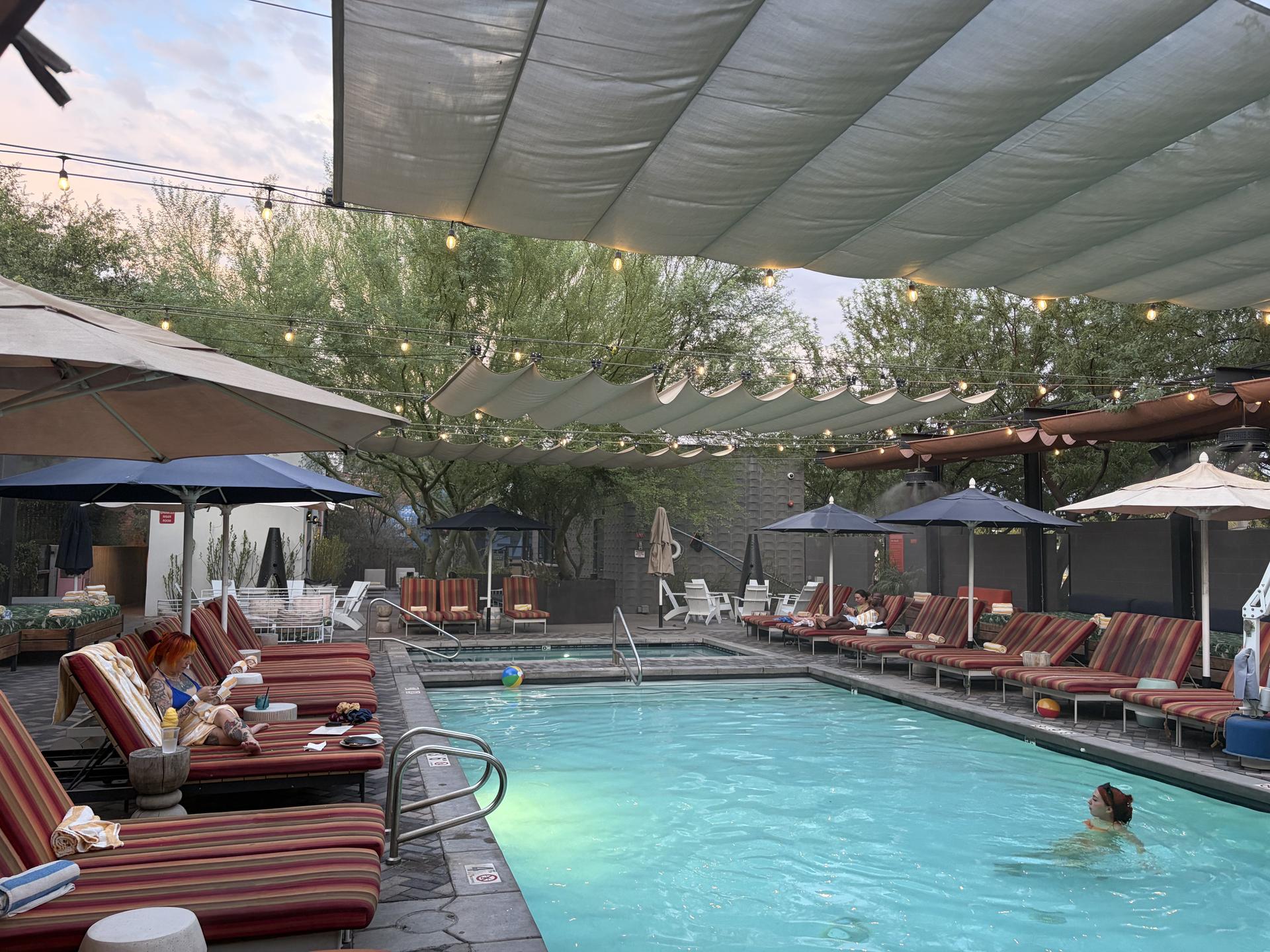 a pool surrounded by lounge chairs and covered with a shade drape