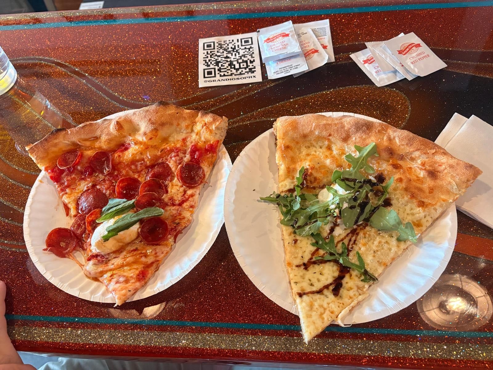 a slice of pepperoni pizza and a slice of white pizza on paper plates on a bar