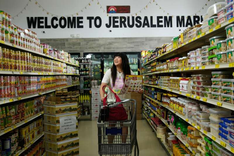 Jenny Yang walking down the aisle of a grocery store pushing a shopping cart